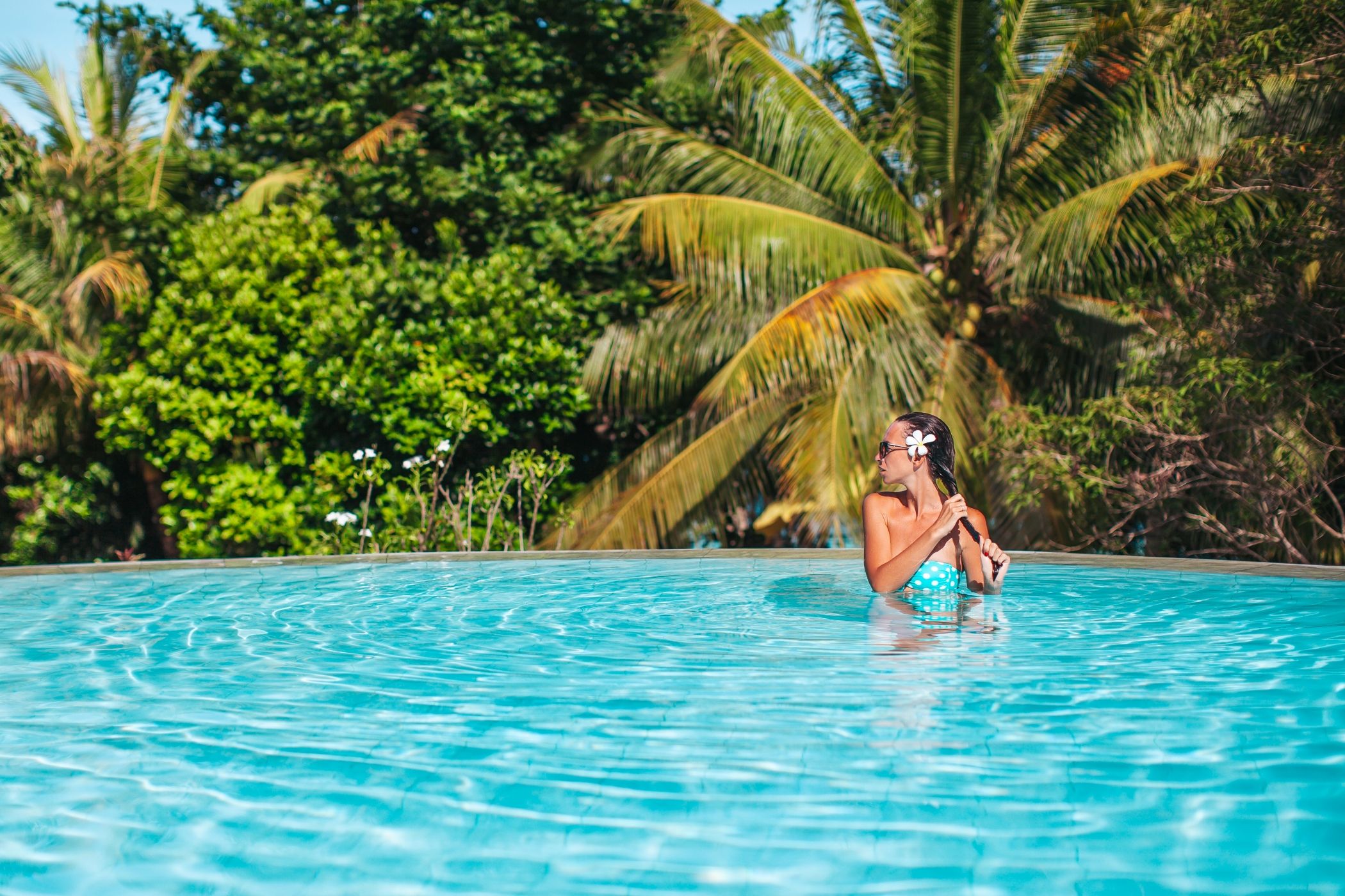 Beautiful young woman relaxing in swimming pool with palm trees behind her in Costa Rica.