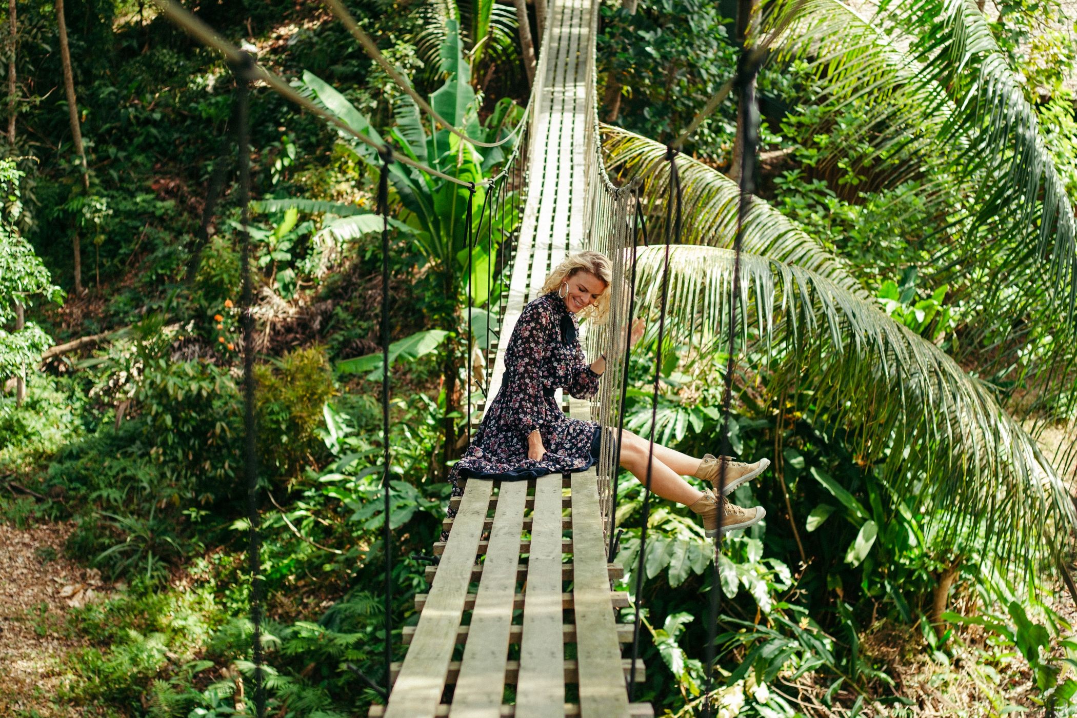 smiling attractive woman sitting on wooden footbridge in a jungle in Costa Rica.