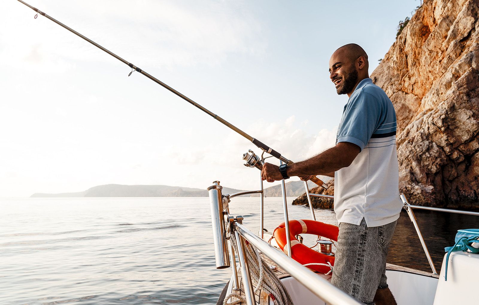 Young African American man standing with fishing rod on a yacht fishing in open sea on Fathers Day.